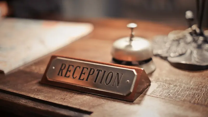 Plaque « Reception » et sonnette posées sur un comptoir d'accueil en bois